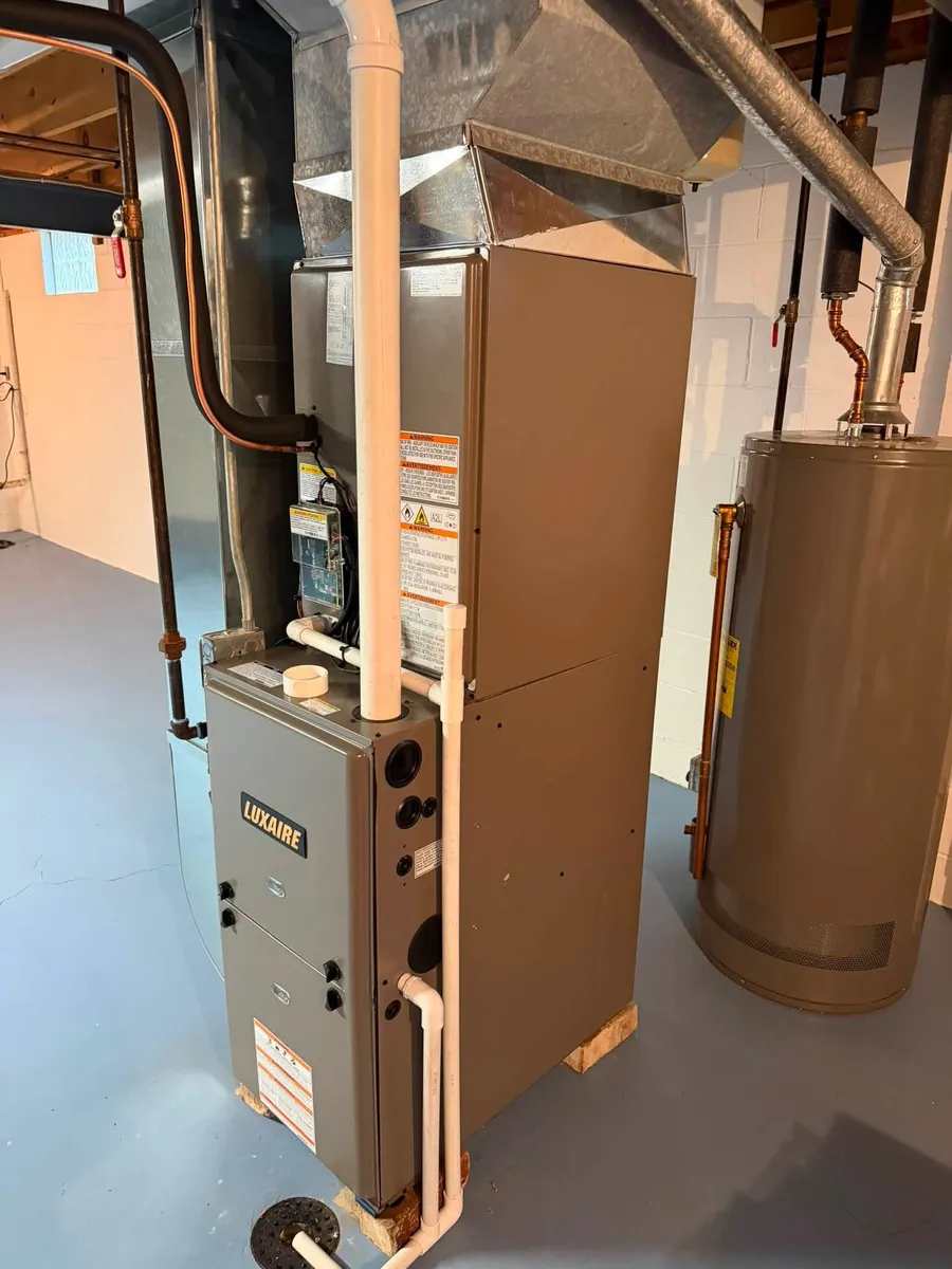 A new high-efficiency furnace in a basement, vented with white plastic pipe, with a plastic drain line running down the side
